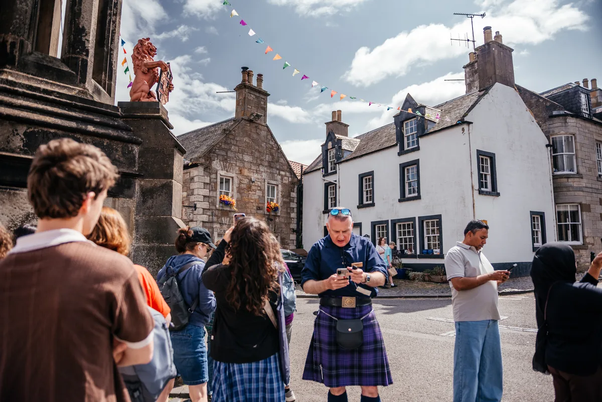 A kilted tour guide with a group in Falkland village square — Outlander's 1945 Inverness